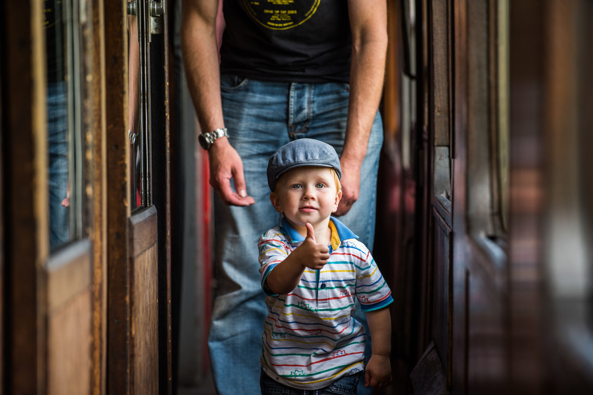 A young boy walks down a train corridor making a thumbs-up sign