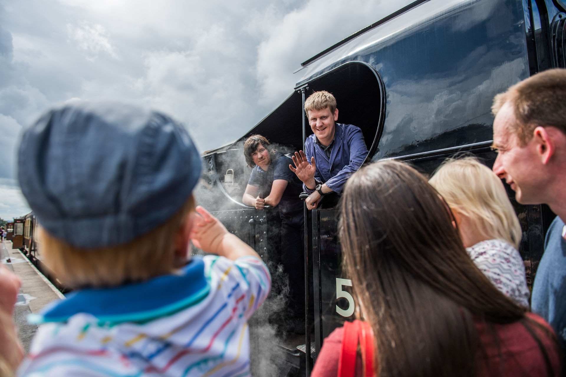 The crew of a steam locomotive wave at a family